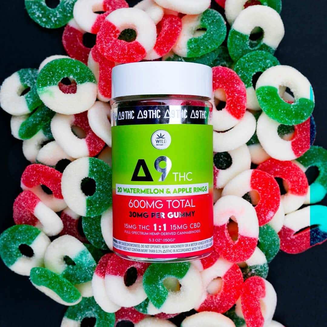 A container of THC-infused watermelon and apple gummy rings, labeled "600mg total, 30mg per gummy," is surrounded by loose edibles.