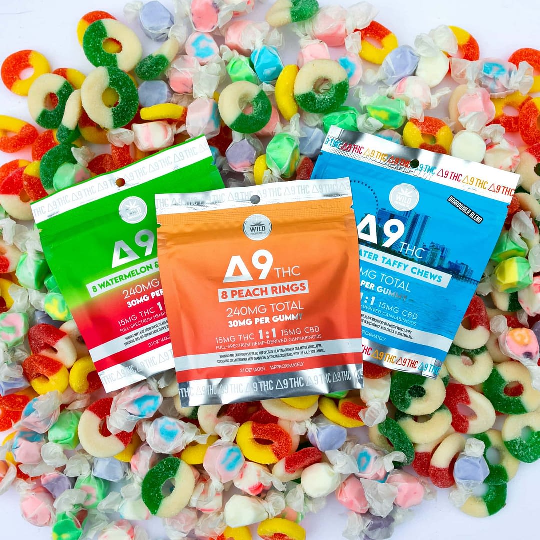 Three colorful bags of Delta 9 THC gummies are displayed on a pile of assorted chewy candies, sharing the spotlight with sleek carts and highlighting the variety of choices in the evolving THCa and THCp market.