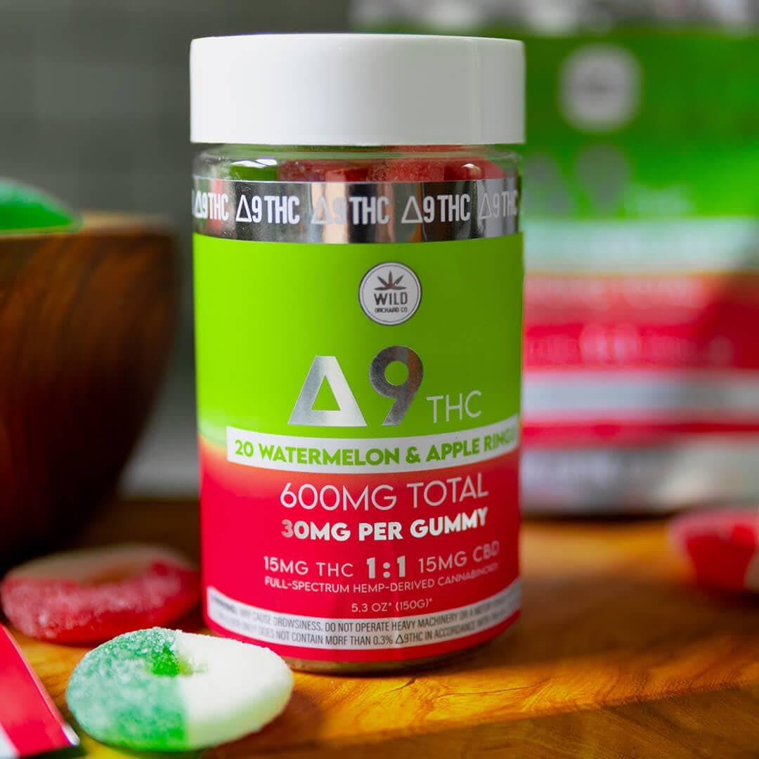 A jar of watermelon and apple flavored gummies stands proudly, showcasing 600mg total Delta 9 THC, CBD, and traces of THCp. Each gummy contains a potent 30mg blend against a subtly blurred backdrop.