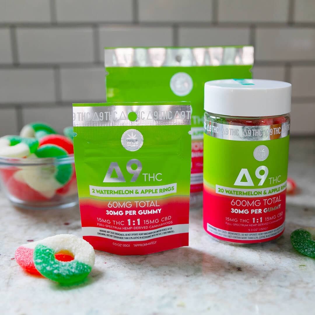 Displayed on the countertop are two packages and a jar of Delta 9 THC watermelon and apple rings, alongside HHC-R-infused gummy rings in a small bowl.