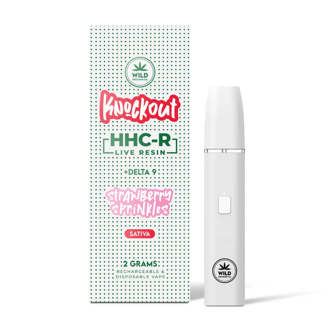 A sleek white vape pen lies beside the box of Knockout “Strawberry Sprinkles” HHC-R Live Resin Vape 2 Gram, labeled with "Delta 9" and "Sativa." Ideal for premium cart fans, it delivers a delightful experience.