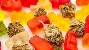 Assorted colorful gummy bears mixed with cannabis buds on a white background evoke a playful contrast, reminiscent of the vibrant experience offered by HHC-R carts.