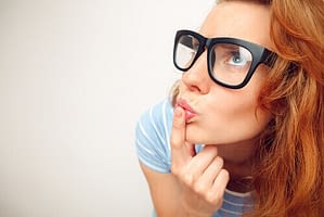 A person with red hair wearing oversized black glasses gazes thoughtfully upwards, fingers gently touching their lips, as if contemplating the nuances of a THCa product.