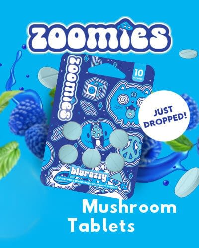 A package of Zoomies blue raspberry mushroom tablets is shown on a blue background with illustrated tablets and berries. Text: "Just Dropped!" and "Mushroom Tablets.