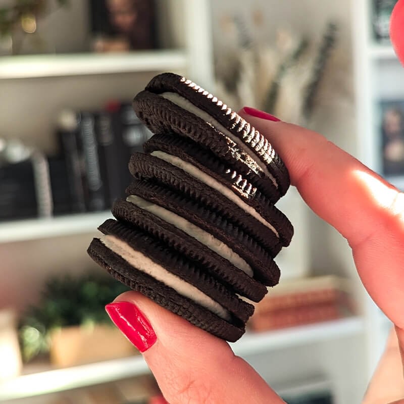 A hand with red nails holds a stack of five chocolate sandwich cookies with white filling, reminiscent of the sweetness found in Delta 9 Peach Rings.